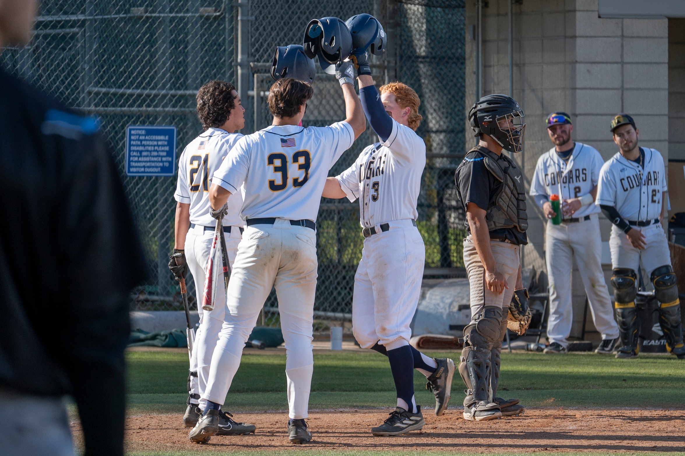 Stock action image of College of the Canyons baseball players Evan Jaquez, Hudson Story and Jake Schwartz meeting at home plate, lifting helmets in the sky, in celebration of a home run during the Cougars' game vs. Moorpark College on Feb. 16, 2024.