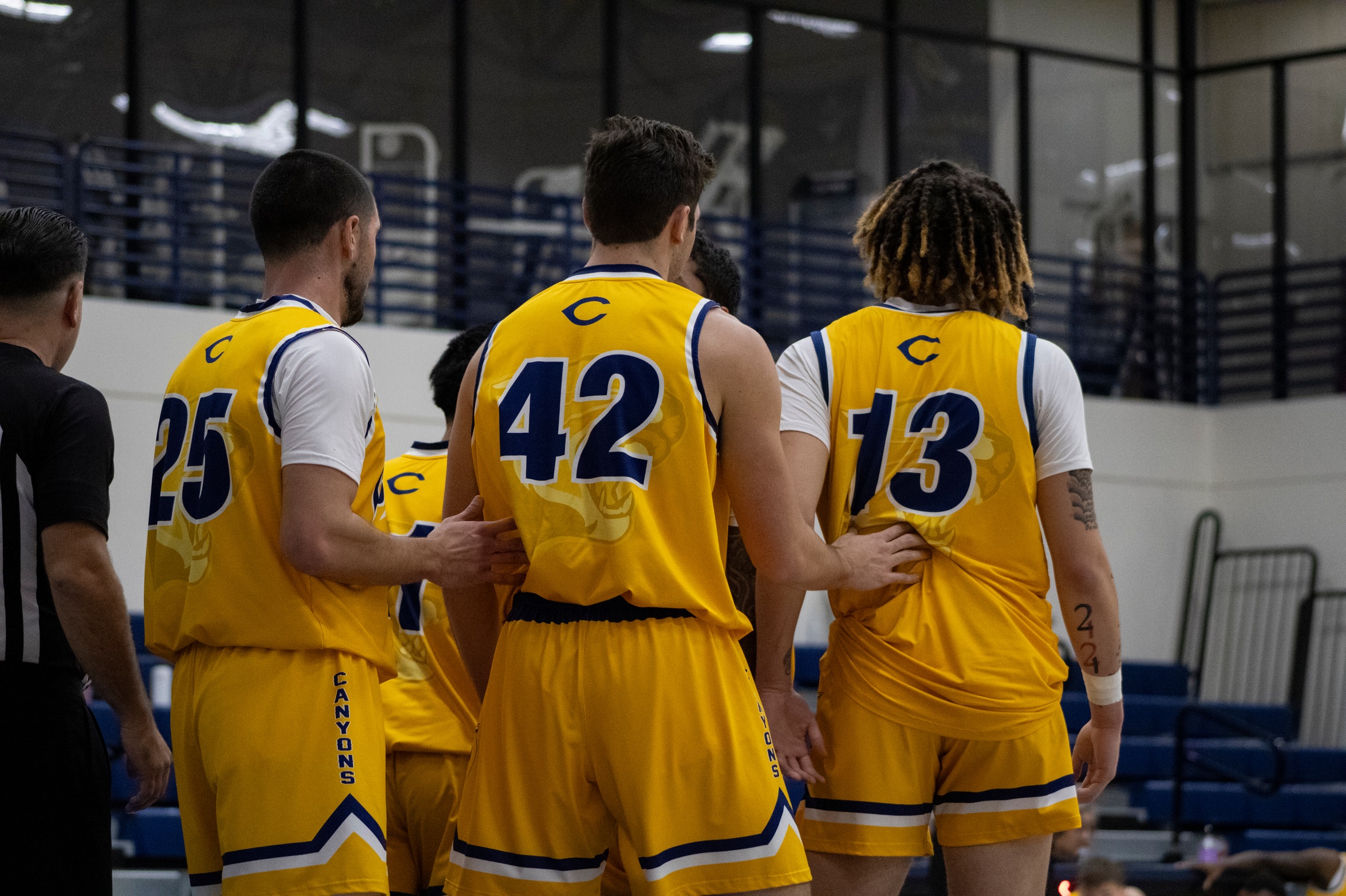 Stock College of the Canyons men's basketball image showing three players in yellow jerseys, with their back to the camera.