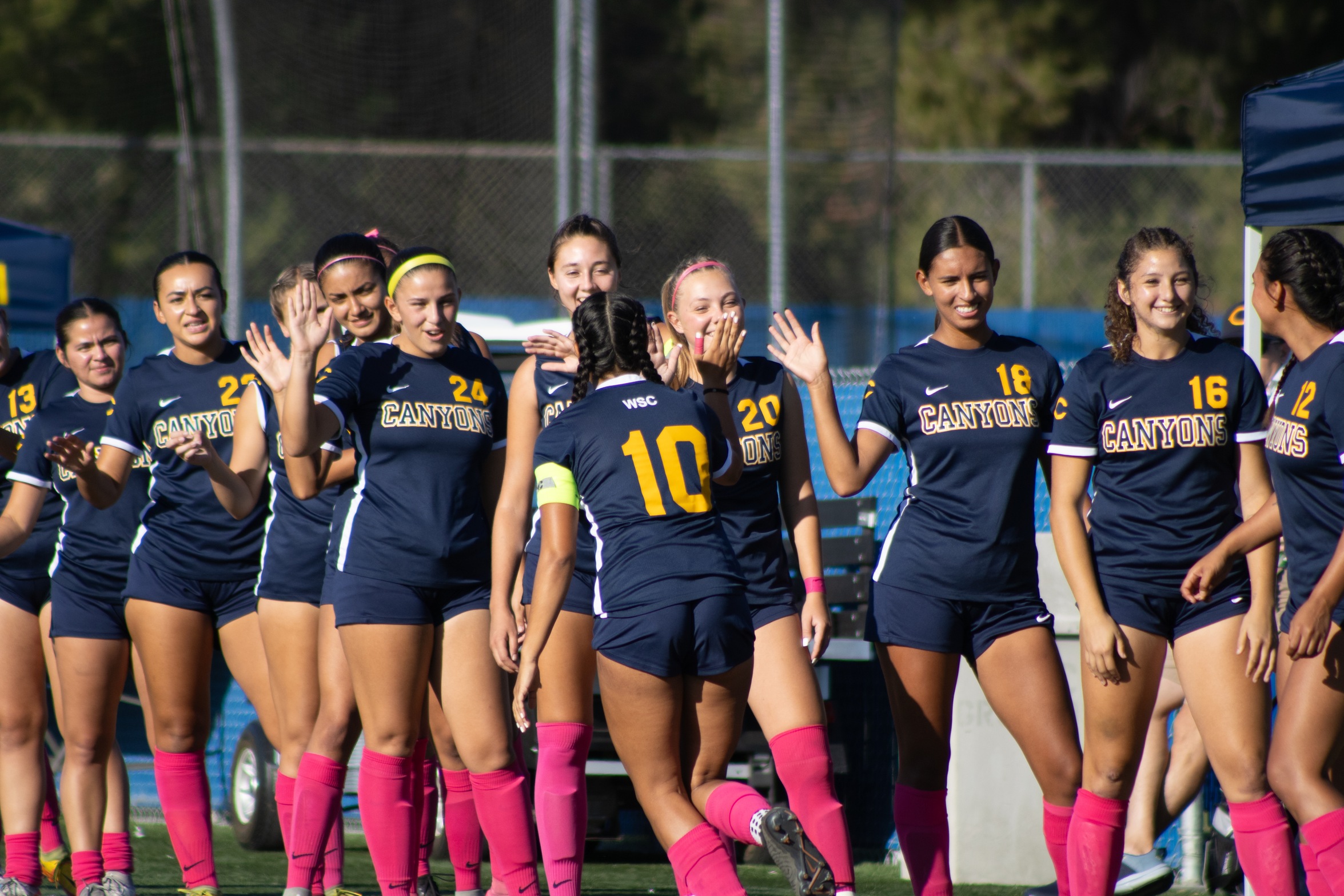 Stock College of the Canyons women's soccer image featuring a player running down a line of other players giving high fives.
